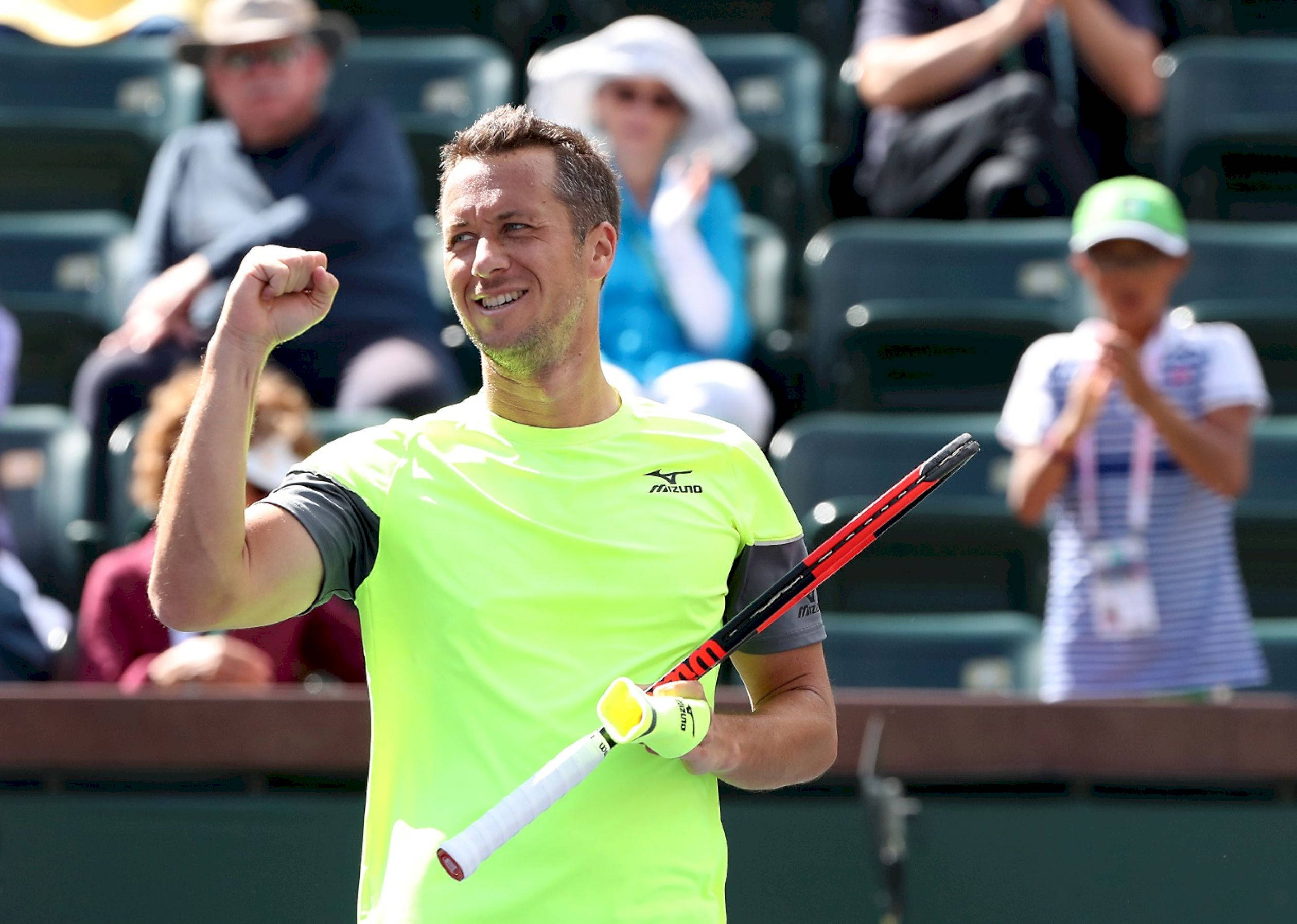 Tennis 桌布 壁紙 — 一名身穿螢光綠色球衣的男網球選手在陽光明媚的球場上握緊拳頭舉起球拍慶祝。