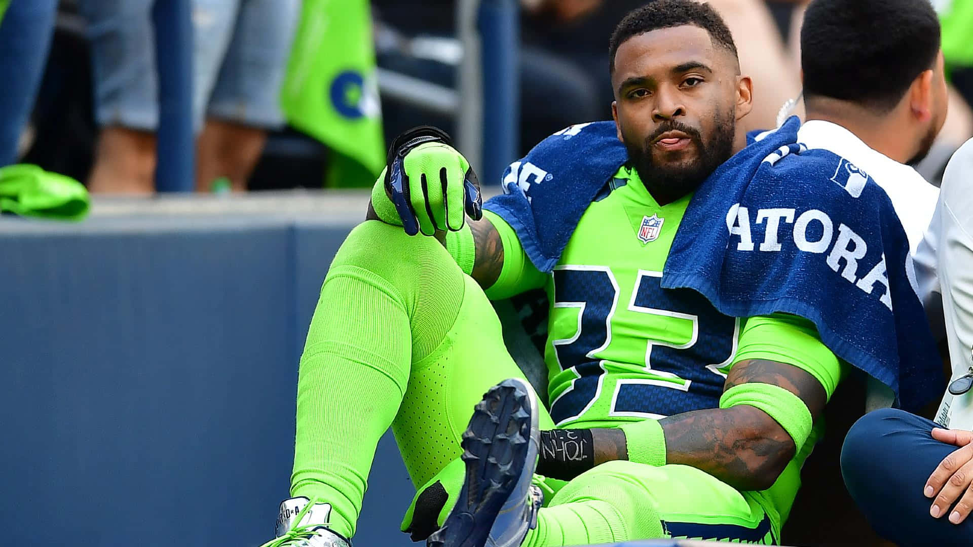 Seattle Seahawks 桌布 壁紙 — 一名身穿螢光綠色球衣的西雅圖海鷹隊美式足球員坐在長凳上，毛巾披在肩上。