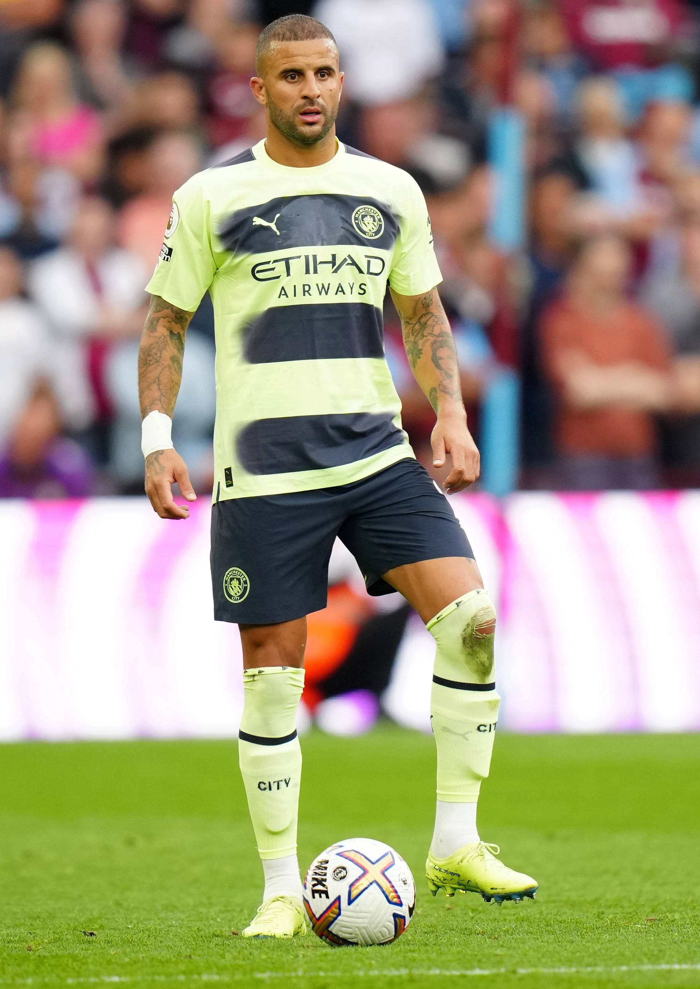 Kyle Walker 桌布 壁紙 — 一名身穿螢光黃和深藍色球衣的足球運動員站在充滿活力的綠色球場上，腳邊有一個足球。