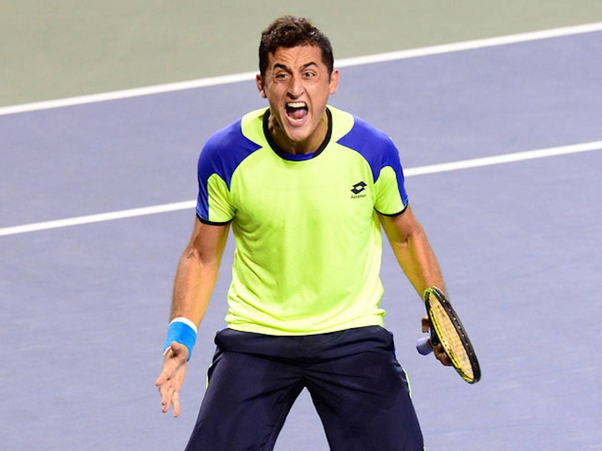 Tennis 桌布 壁紙 — 一名身穿螢光黃和藍色襯衫的男網球運動員在紫色硬地球場上高舉球拍，勝利地吶喊。