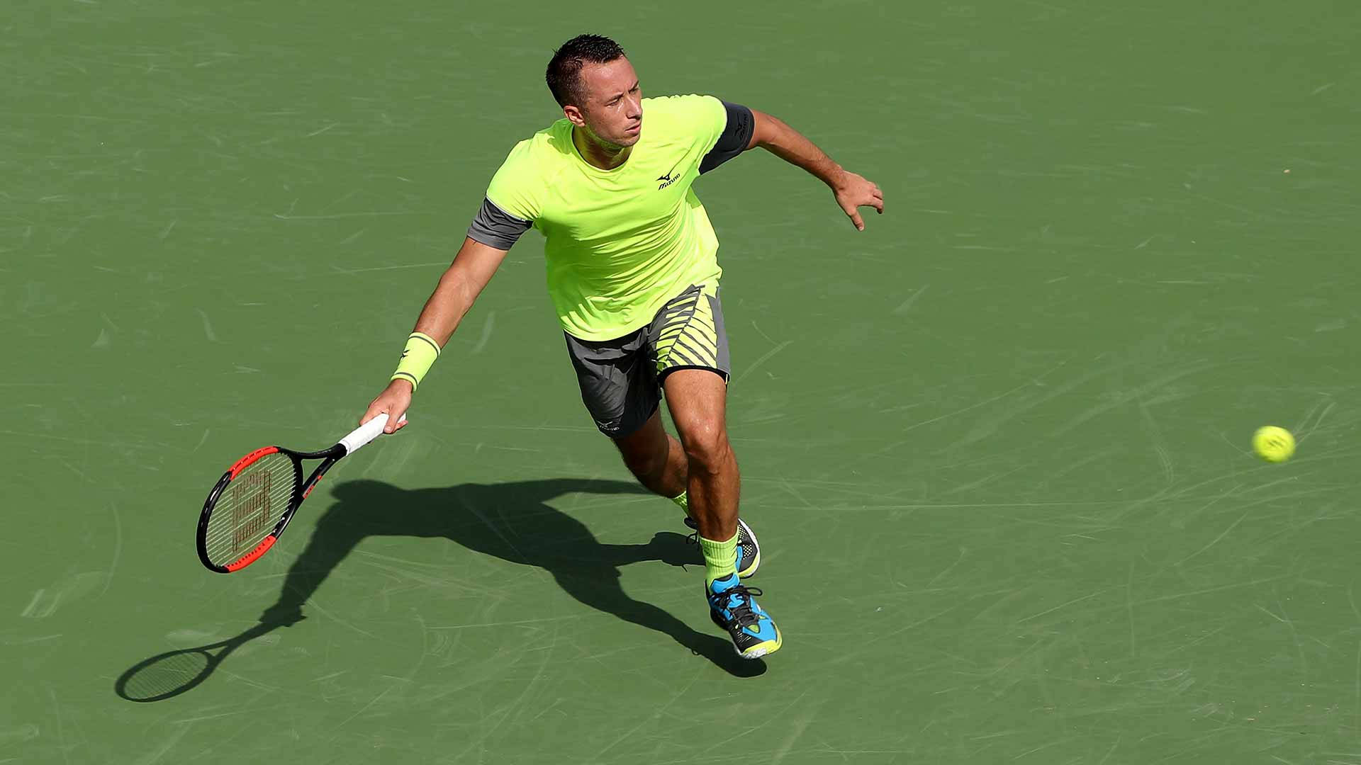 Athlete 桌布 壁紙 — 一名身穿螢光黃色球衣的男網球選手在綠色球場上向前撲出，擊打一個亮黃色的球。