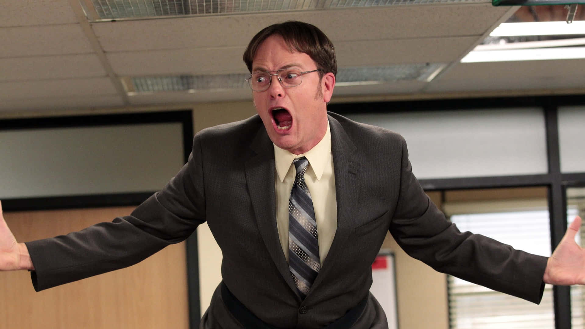 rainn wilson 桌布 壁紙 — 一名身穿西裝、戴眼鏡的男子在螢光燈照明的辦公室隔間內張開雙臂尖叫。