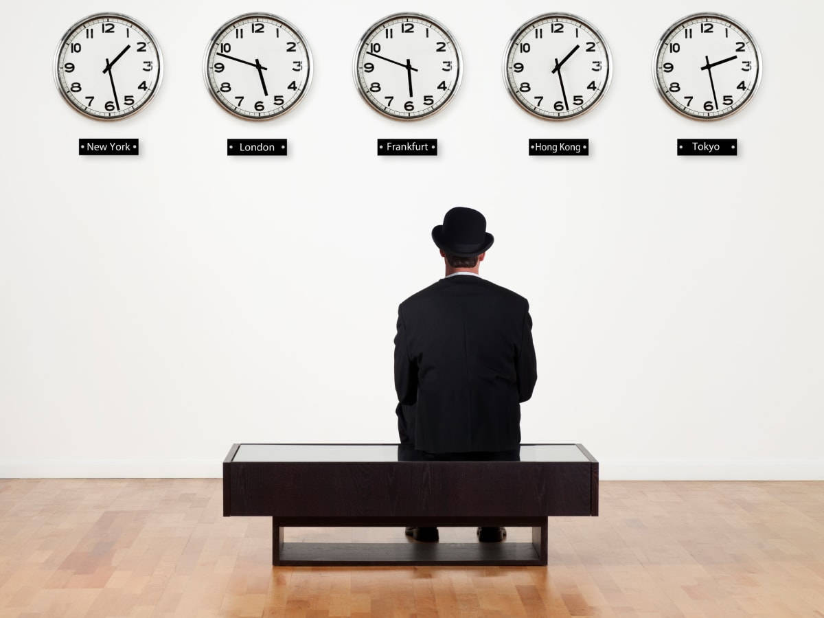Clocks 桌布 壁紙 — 一名身穿西裝戴著圓頂禮帽的男子坐在長椅上，面對五個標有全球城市名稱、顯示不同時間的掛鐘。