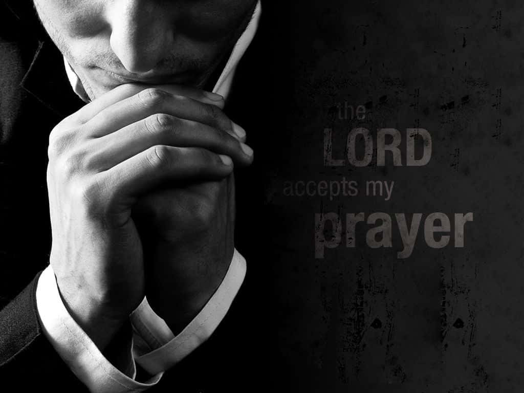 Praying 桌布 壁紙 — 一名身穿西裝的男子，雙手合十，對著一面深色紋理牆壁祈禱，牆上有粗糙字體寫著「the LORD accepts my prayer」。