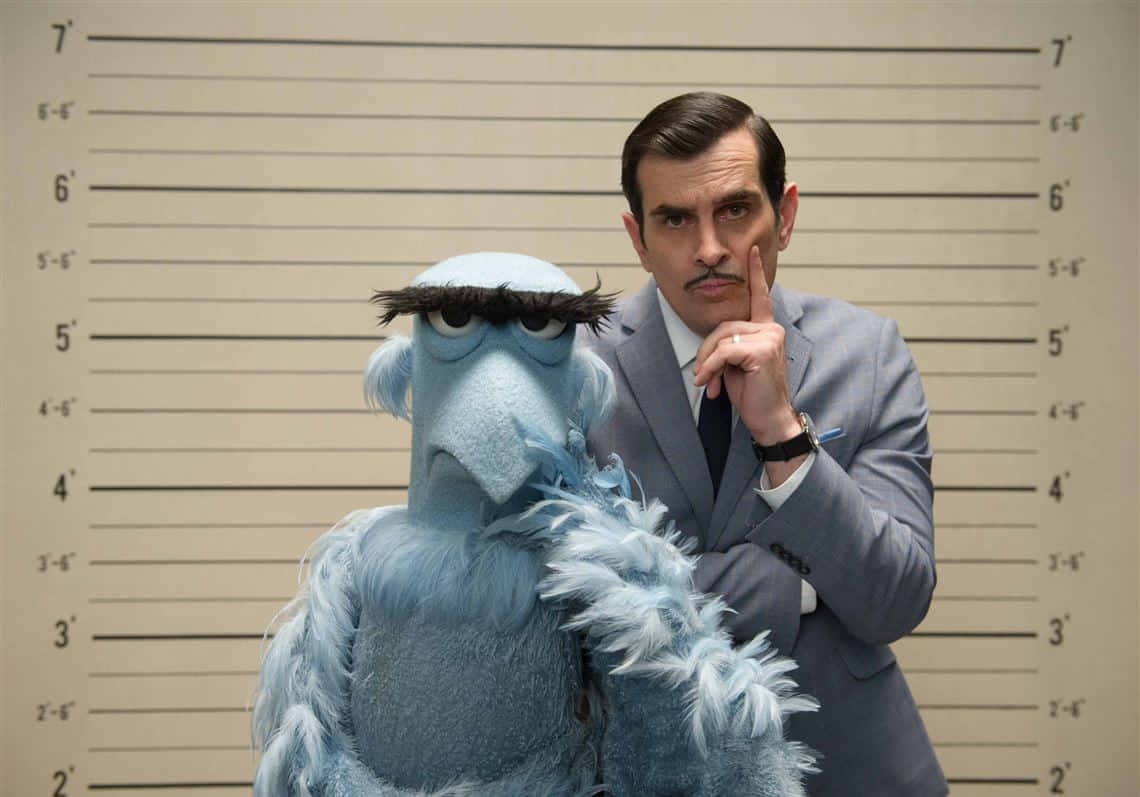 Ty Burrell 桌布 壁紙 — 一名身穿西裝的男子和一個藍色毛絨玩偶在身高圖表前擺姿勢拍攝入案照。