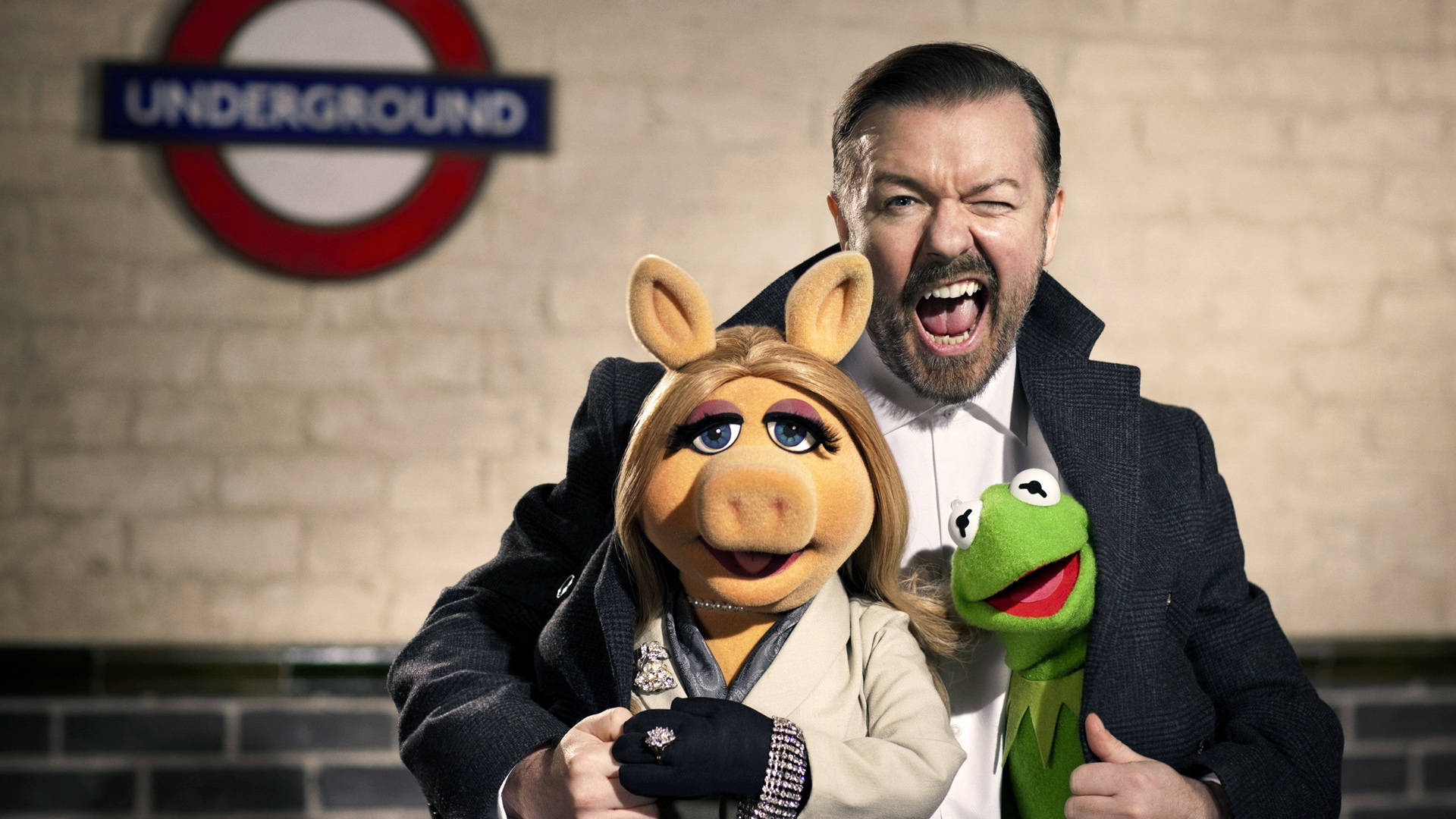 muppets 桌布 壁紙 — 一名身穿西裝的男子在倫敦地鐵標誌前狂笑，同時抱著豬小姐和青蛙科米。