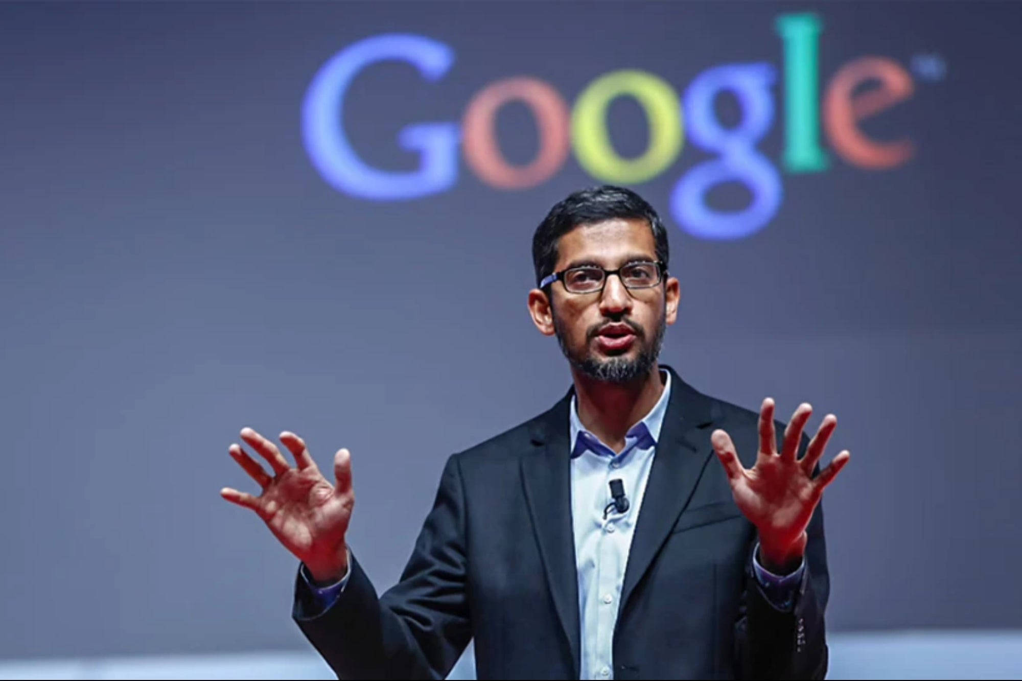 google 桌布 壁紙 — 一名身穿西裝的男子在台上發言時做手勢，身後有色彩繽紛的Google標誌。
