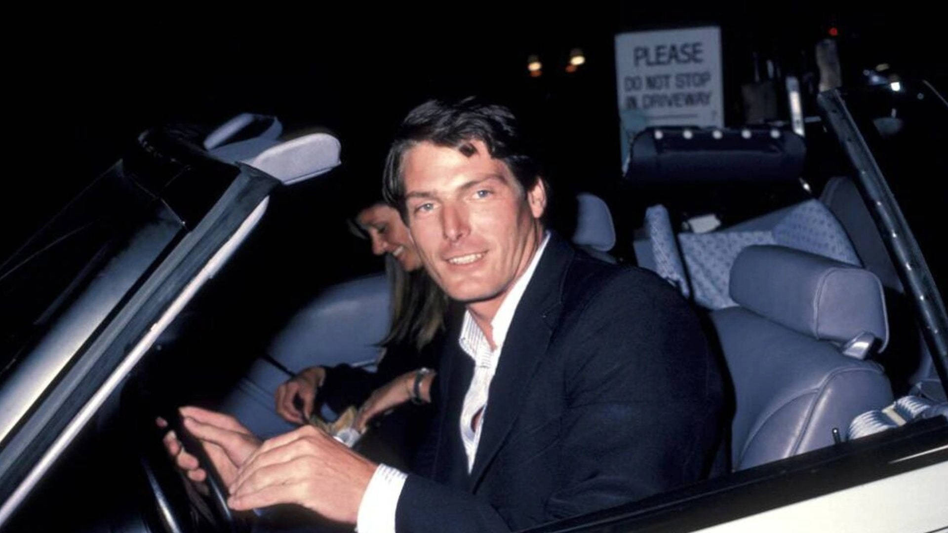 Christopher 桌布 壁紙 — 一名身穿西裝的男子在夜間從敞篷車的駕駛座上微笑，旁邊有一位女士。