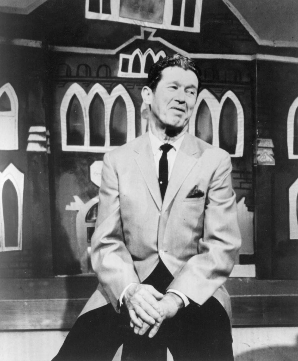 Singer 桌布 壁紙 — 一名身穿西裝的男子在復古黑白照片中，平靜地坐在風格化的卡通屋背景前。