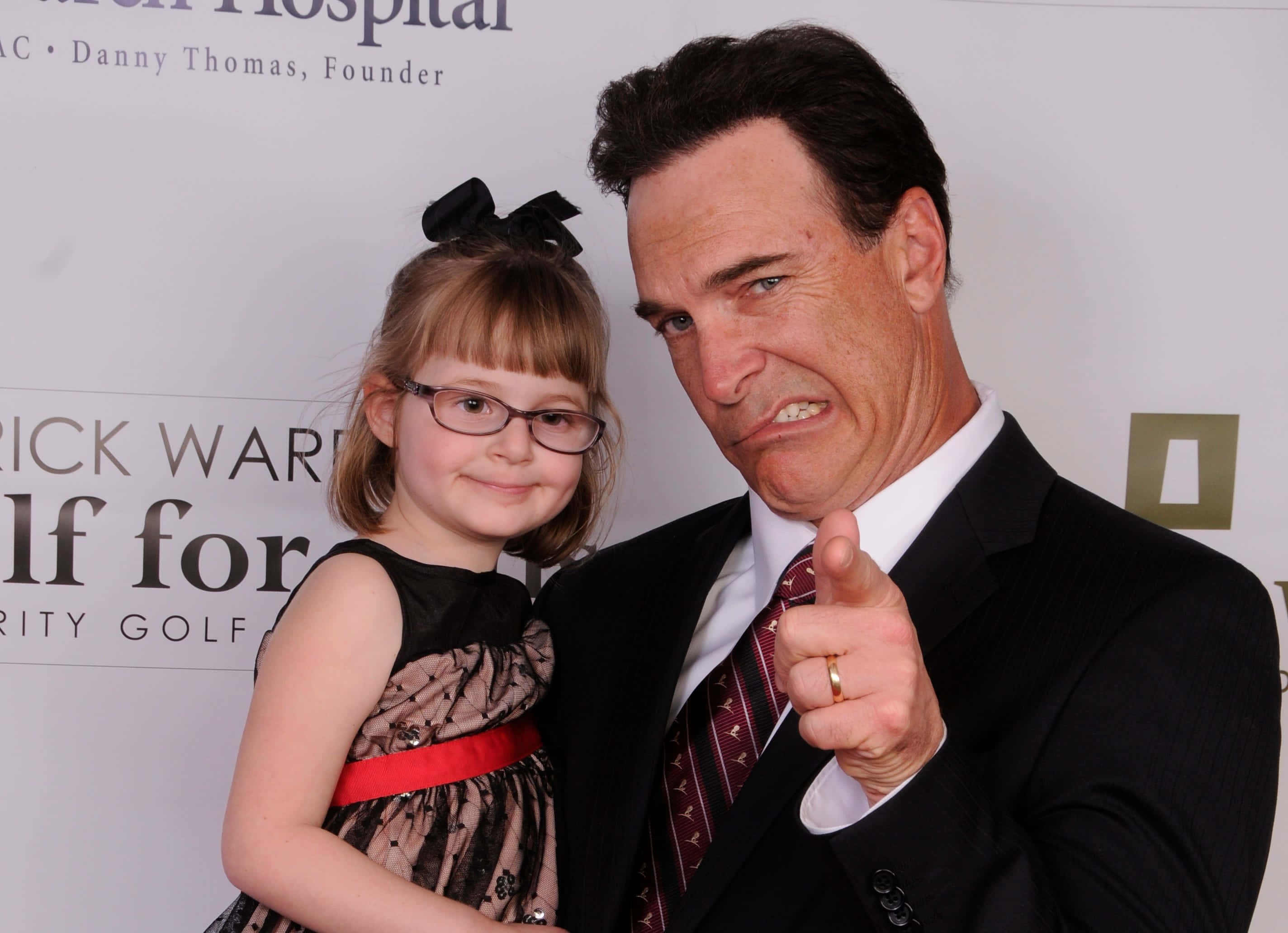 Patrick Warburton 桌布 壁紙 — 一名身穿西裝的男子在戴眼鏡和穿連衣裙的微笑年輕女孩旁邊，對著鏡頭做鬼臉並指向相機。