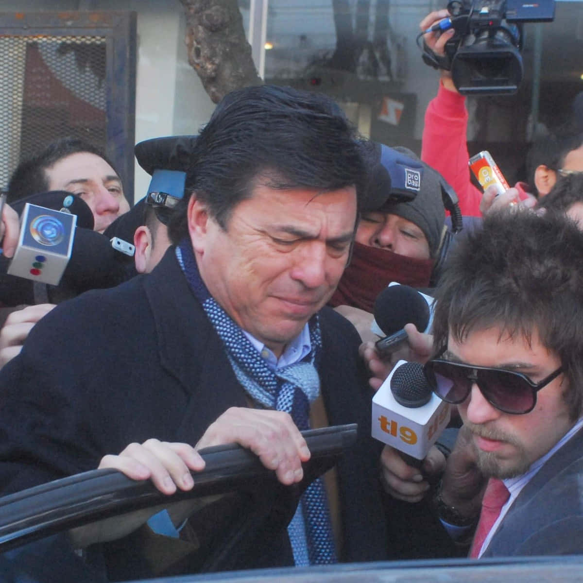 Celebrity 桌布 壁紙 — 一名身穿西裝的男子在擠滿記者和攝影機的繁忙城市街道上，從車窗探出身子。