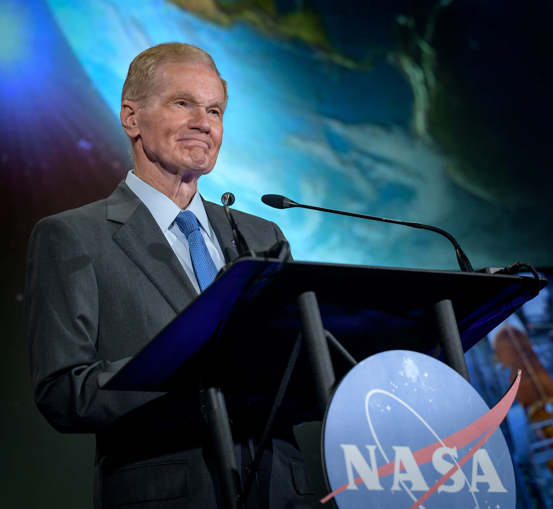  壁紙 — 一名身穿西裝的男子在正式演講中站在NASA講台上，背景是宇宙星空。