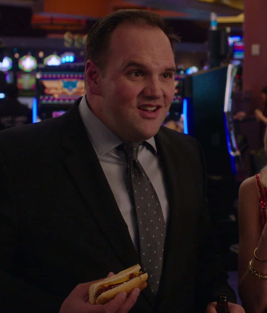 Ethan Suplee 桌布 壁紙 — 一名身穿西裝的男子在燈光昏暗的賭場中拿著熱狗和啤酒，身後是發光的老虎機。