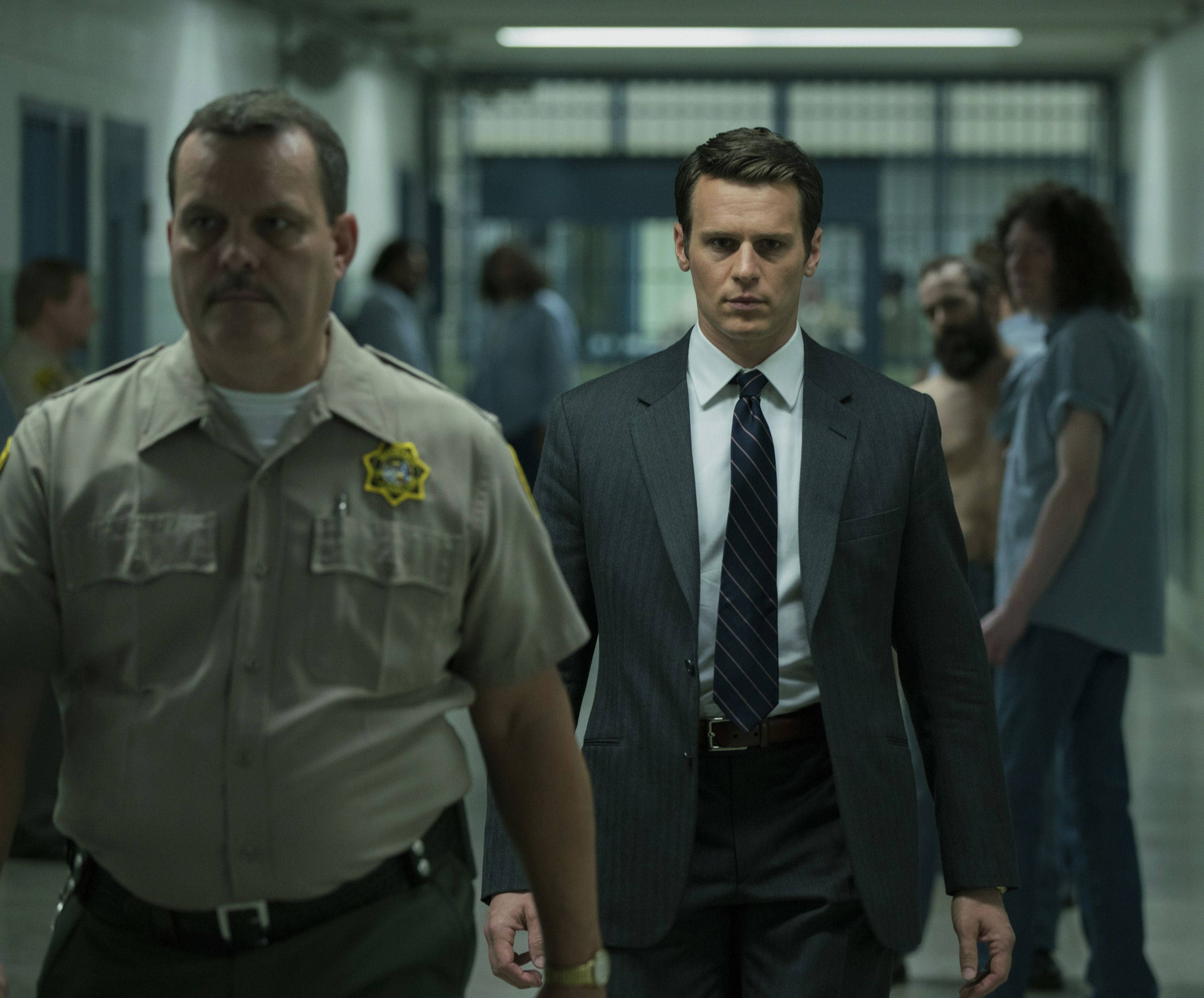 Netflix 桌布 壁紙 — 一名身穿西裝的男子在監獄走廊行走，兩旁有警衛和背景中的囚犯。