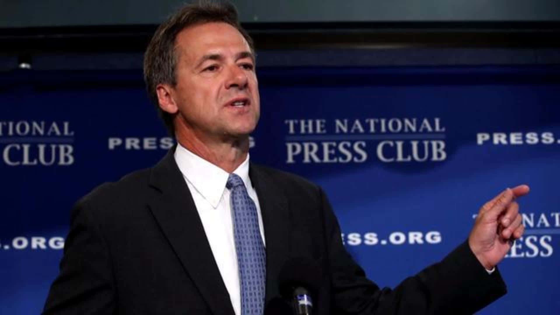 政治 桌布 壁紙 — 一名身穿西裝的男子在藍色「National Press Club」背景前的講台上發言並做手勢。