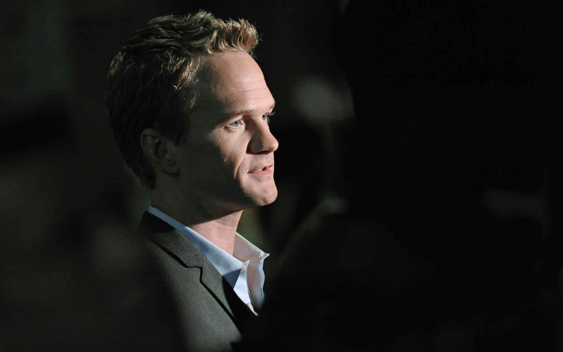 neil patrick harris 桌布 壁紙 — 一名身穿西裝的男子在黑暗模糊的背景中被戲劇性的側光照亮。