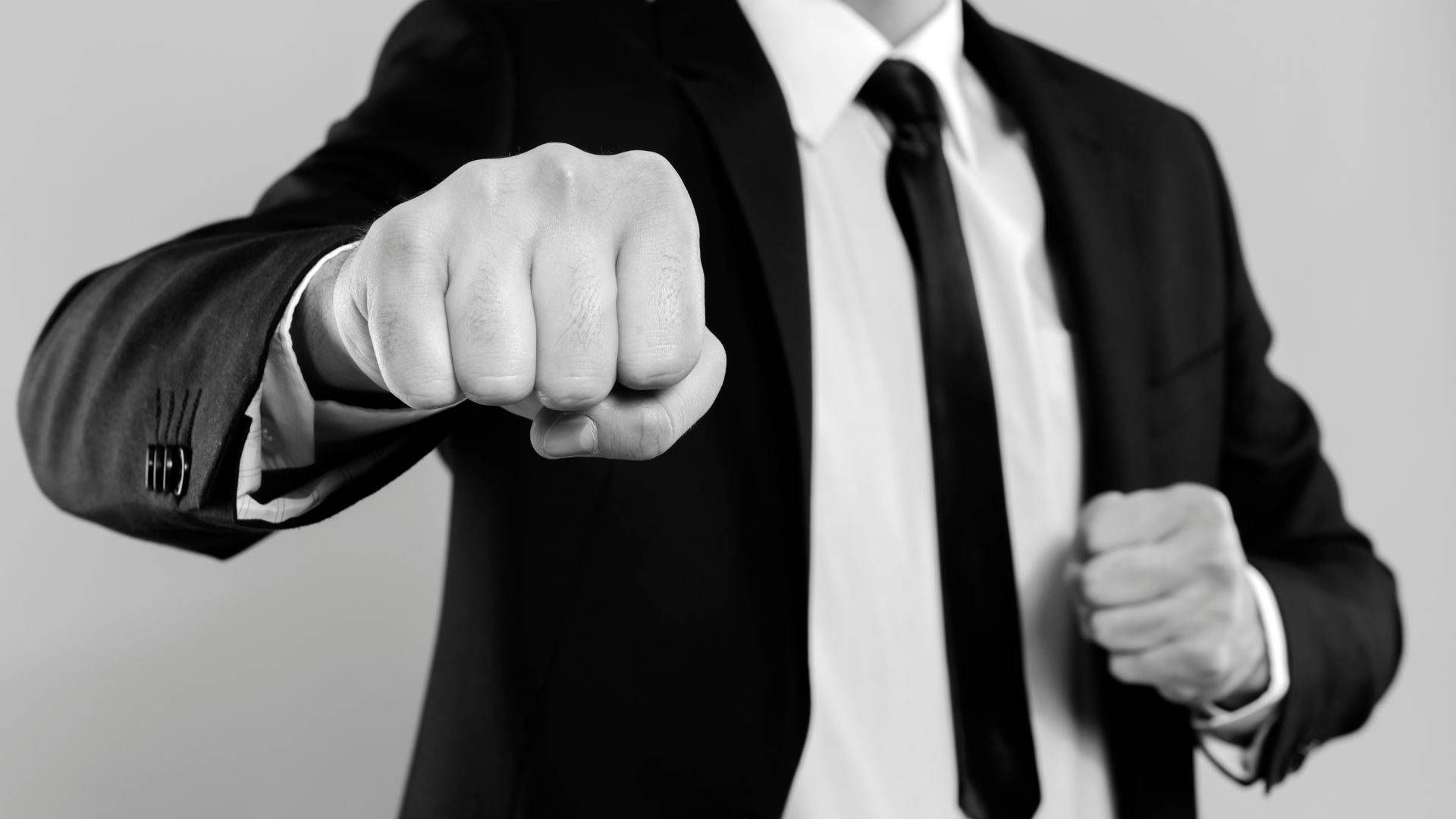 Power 桌布 壁紙 — 一名身穿西裝的男子在黑白工作室照片中向前揮出緊握的拳頭。