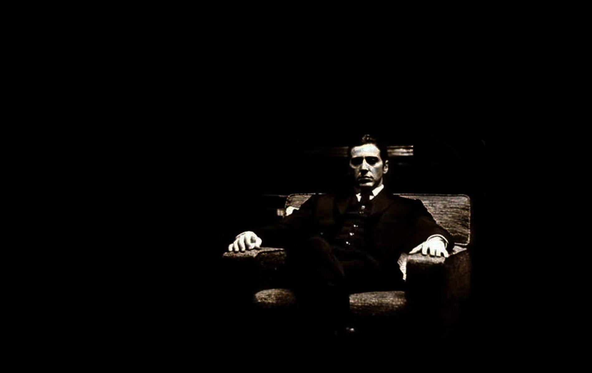 Godfather 桌布 壁紙 — 一名身穿西裝的男子坐在椅子上，被戲劇性的聚光燈照射，背景漆黑一片。