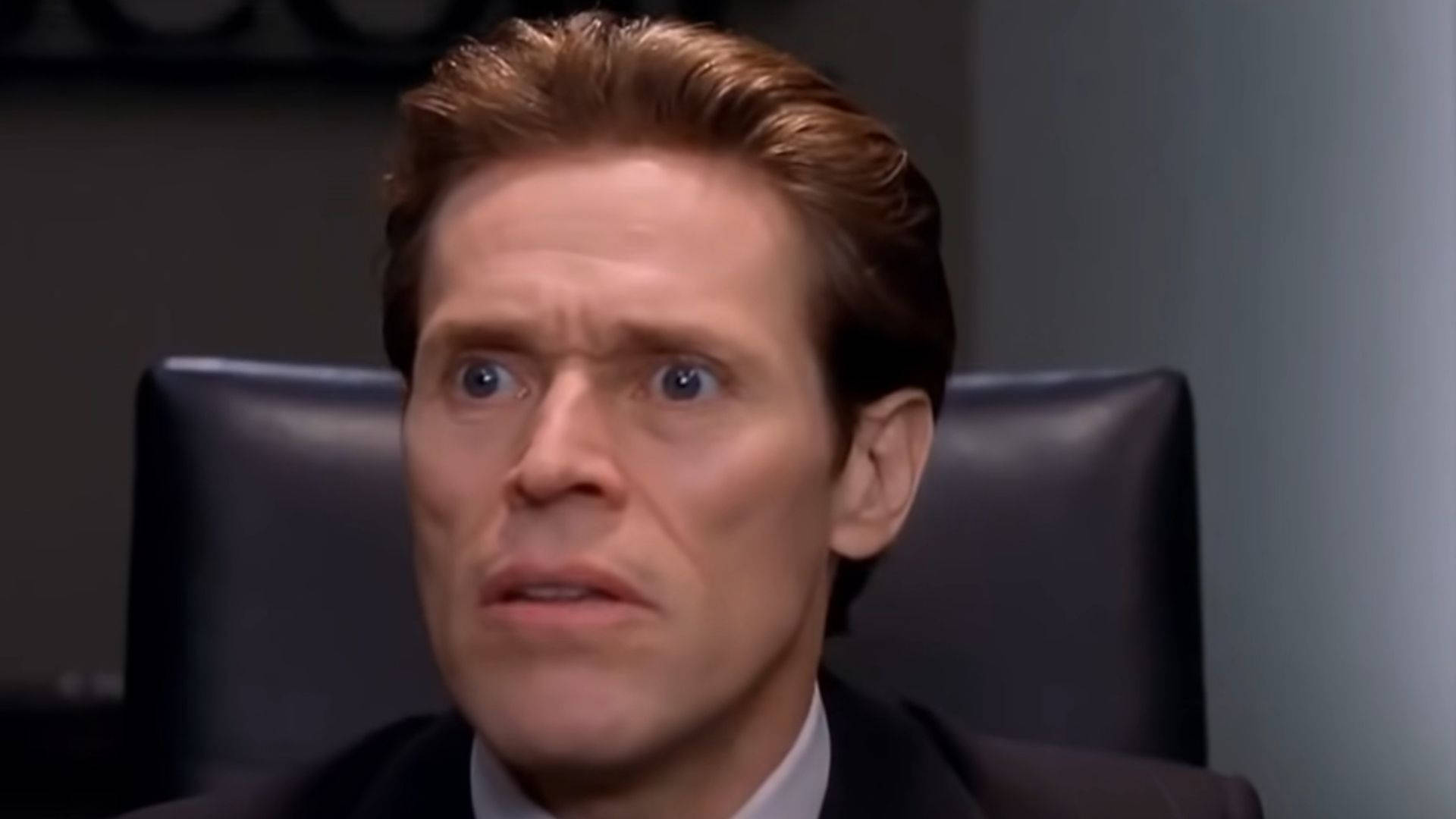 Willem Dafoe 桌布 壁紙 — 一名身穿西裝的男子坐在皮椅上，睜大眼睛，表情震驚，在燈光昏暗的辦公室裡。