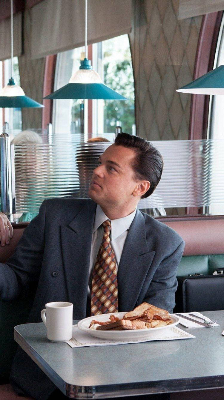 Wolf Of Wall Street 桌布 壁紙 — 一名身穿西裝的男子坐在餐廳餐桌旁，在青綠色吊燈下享用早餐。