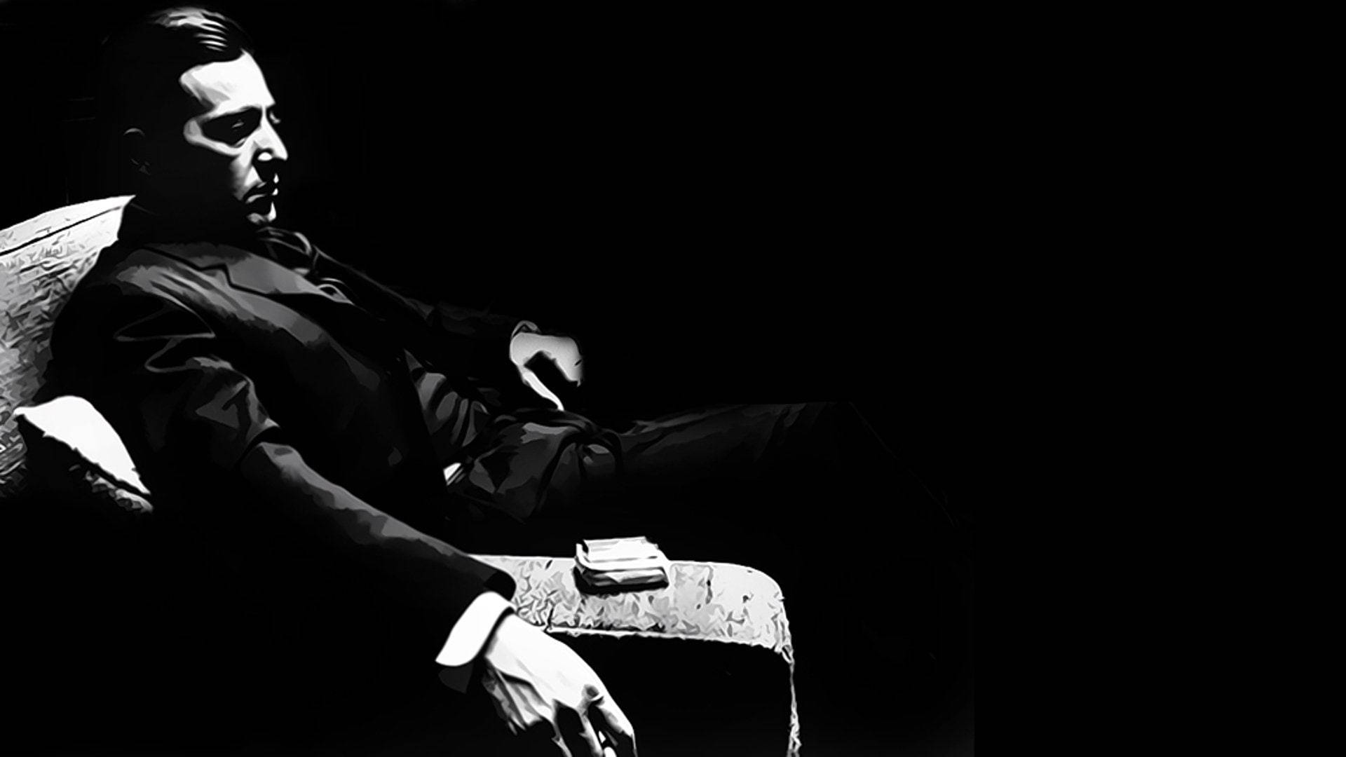 Godfather 桌布 壁紙 — 一名身穿西裝的男子坐在黑暗房間的椅子上，戲劇性的燈光突顯他的側面和雙手。