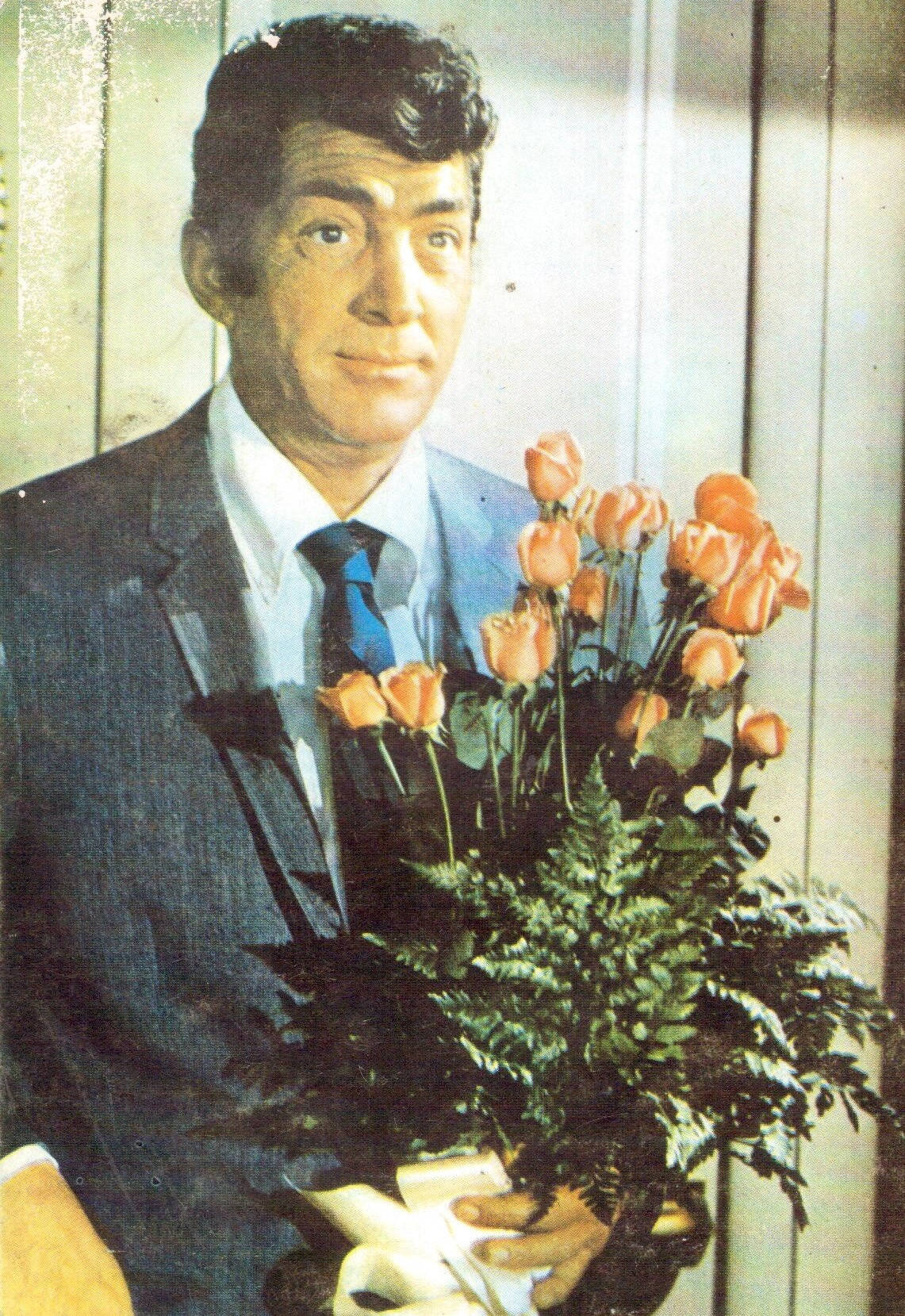 Painting 桌布 壁紙 — 一名身穿西裝的男子手持一束橙色玫瑰和蕨類植物，背景是淺色木鑲板牆。