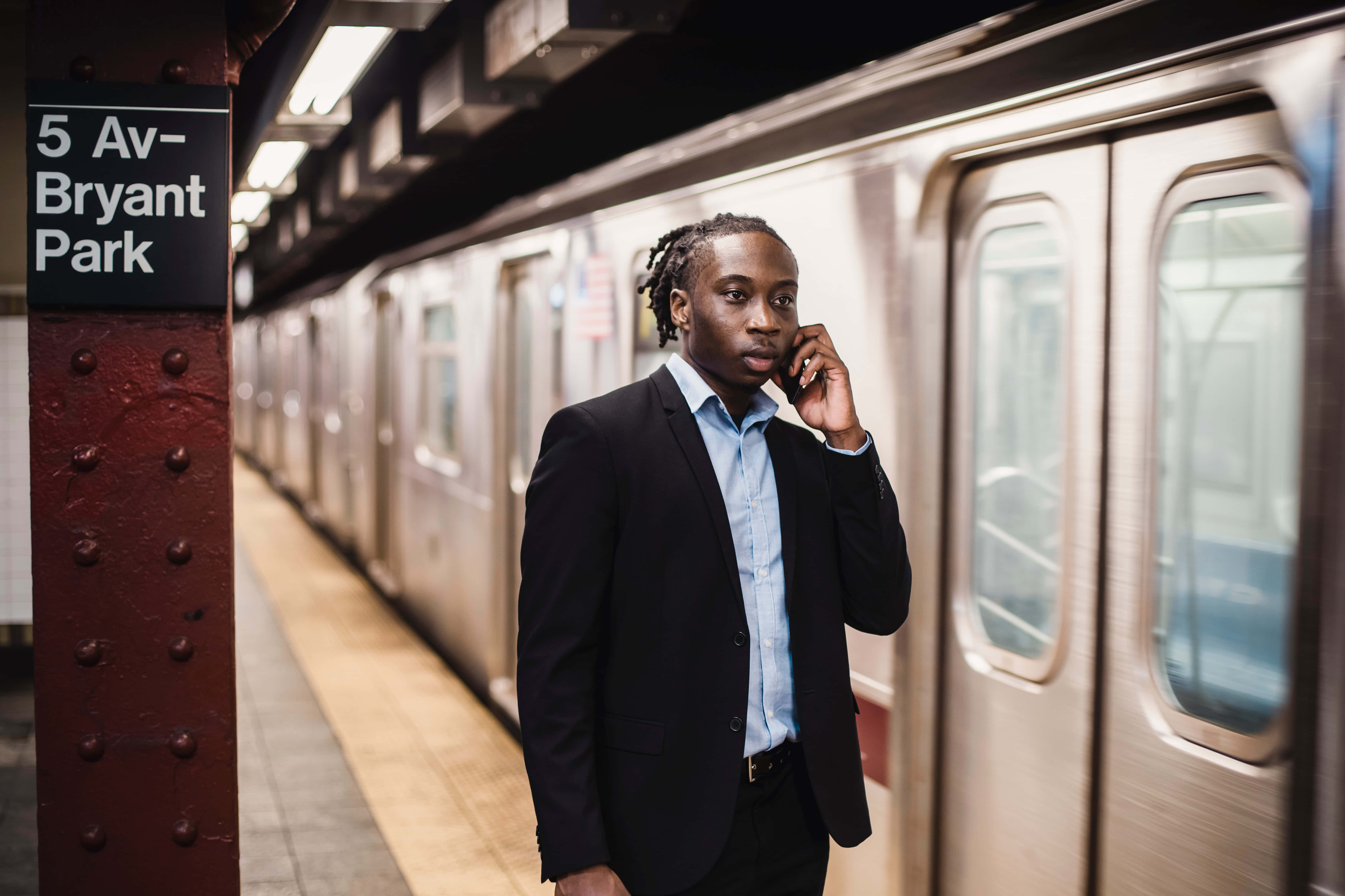 Nyc 桌布 壁紙 — 一名身穿西裝的男子站在5 Av-Bryant Park車站的地鐵月台上，一邊講電話，一邊看著列車駛過。