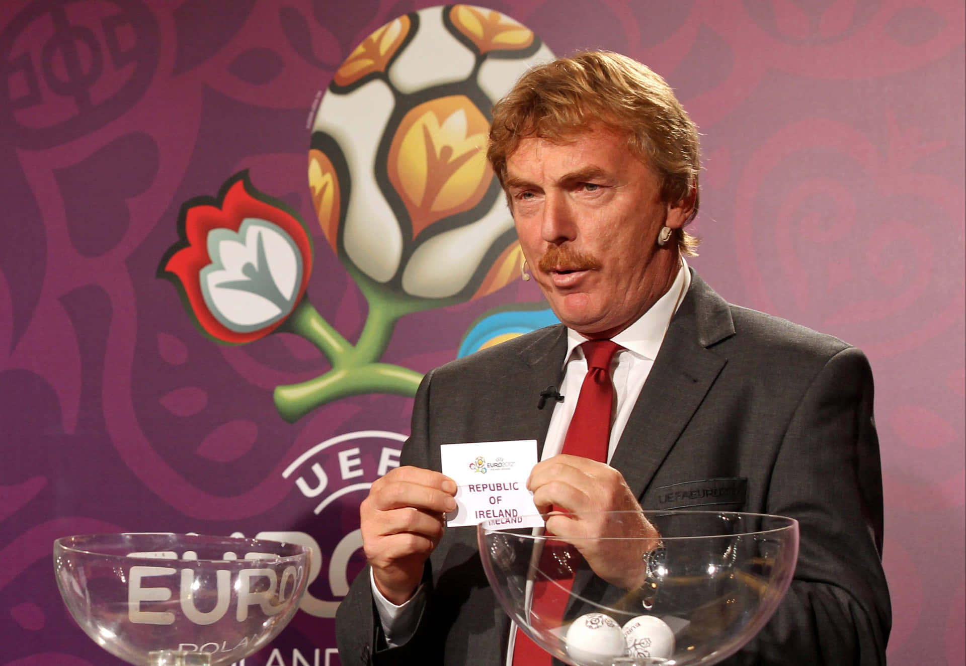 足球 桌布 壁紙 — 一名身穿西裝的男子站在帶有足球標誌的UEFA Euro 2012品牌背景前，手持寫有Republic of Ireland的卡片。