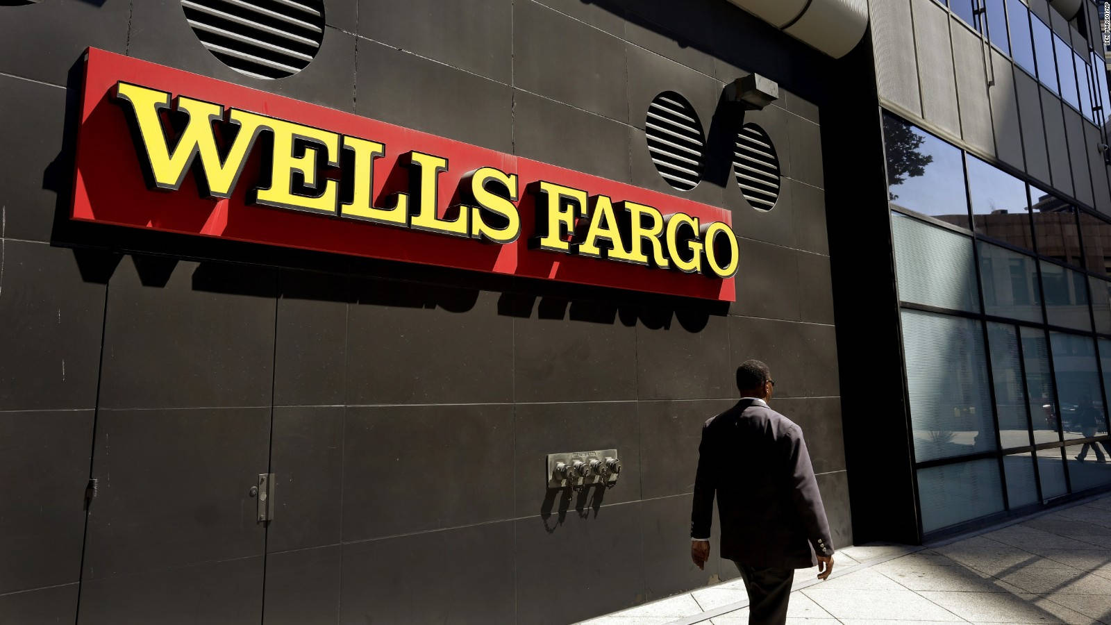 標誌 桌布 壁紙 — 一名身穿西裝的男子走過 Wells Fargo 銀行大樓，大樓有醒目的紅黃色標誌，背景是深灰色牆壁。
