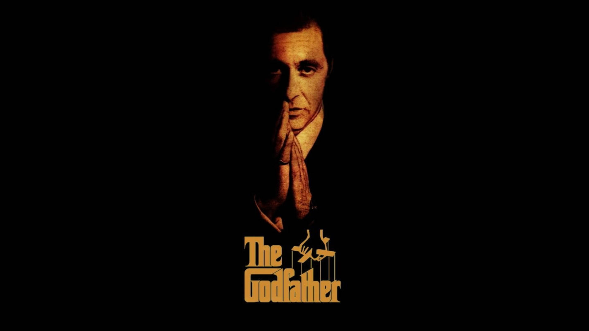 Godfather 桌布 壁紙 — 一名身穿西裝的男子雙手合十靠近臉部，在黑色背景上被溫暖光線照亮，下方有『The Godfather』標題。