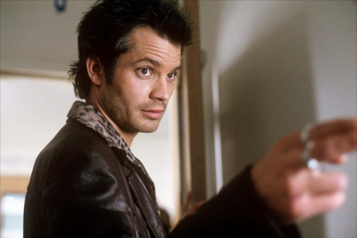 timothy olyphant 桌布 壁紙 — 一名身穿豹紋領皮夾克的男子，在柔和光線的室內環境中，表情嚴肅地向前指。
