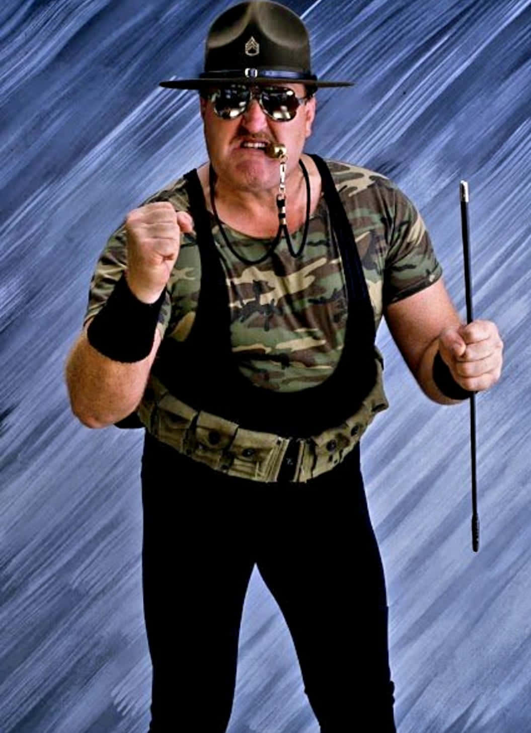 WWE 桌布 壁紙 — 一名身穿軍裝、戴著太陽眼鏡的男子，在藍色條紋背景前，手持手杖，擺出帶有攻擊性的姿勢。