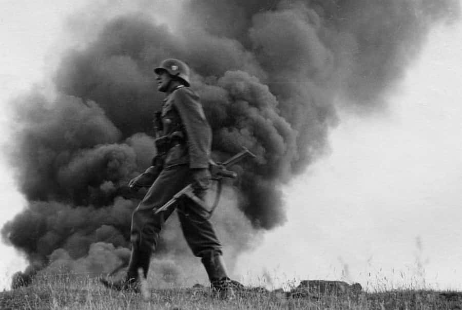 soldier 桌布 壁紙 — 一名身穿軍裝的士兵走過草地，背後濃煙滾滾，照片為清晰的黑白風格。