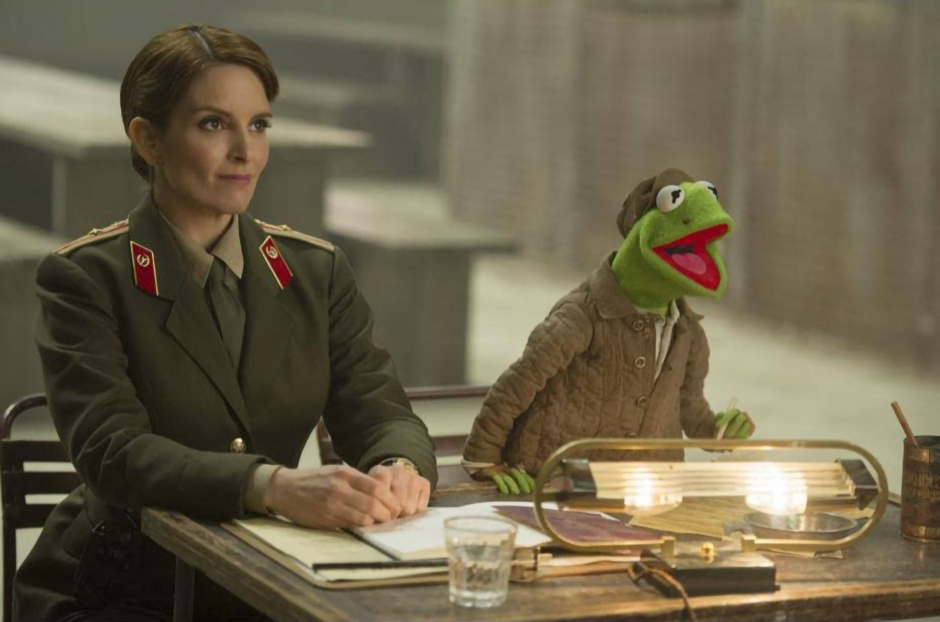 muppets 桌布 壁紙 — 一名身穿軍裝的女子與青蛙柯密特坐在一張桌子旁，處於一個緊張、燈光昏暗的審訊室中。