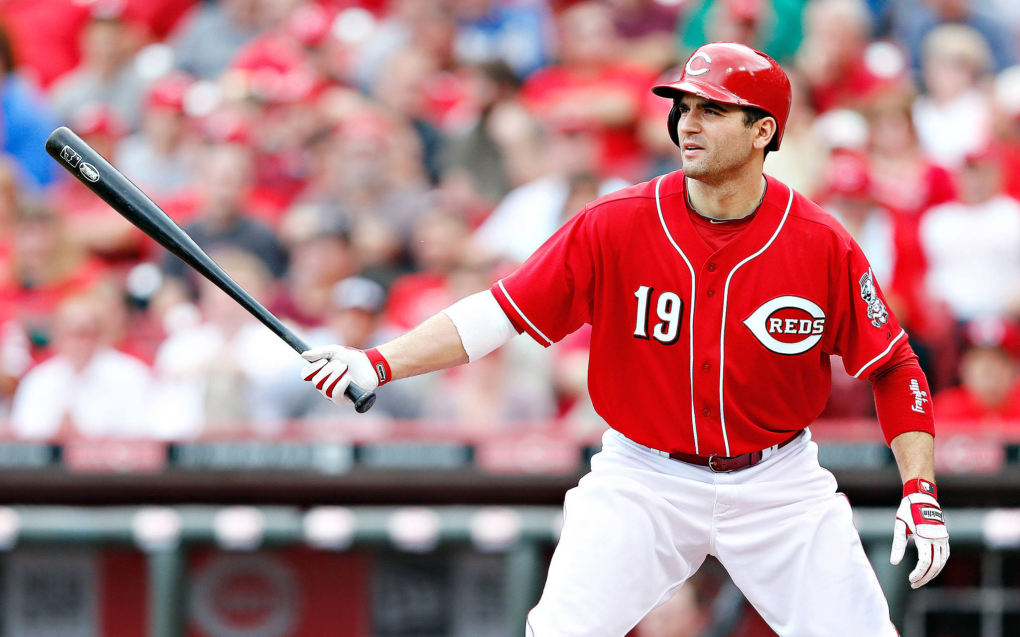 Joey Votto 桌布 壁紙 — 一名身穿辛辛那提紅人隊紅色球衣的棒球選手在日間比賽中揮棒，背景是模糊的人群。