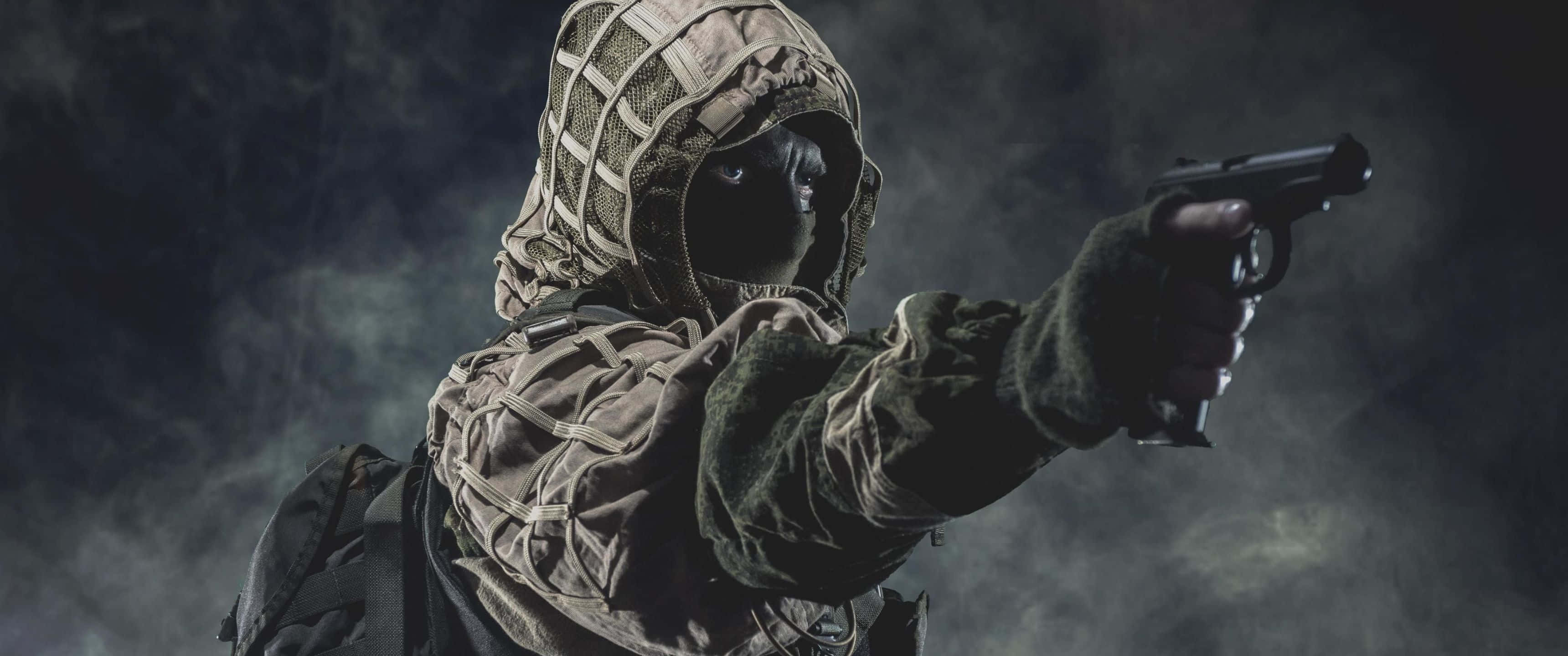 3440x1440p Rainbow Six Siege 桌布 壁紙 — 一名身穿迷彩服和巴拉克拉瓦頭套的士兵，在煙霧瀰漫的黑暗背景下，專注地瞄準手槍。