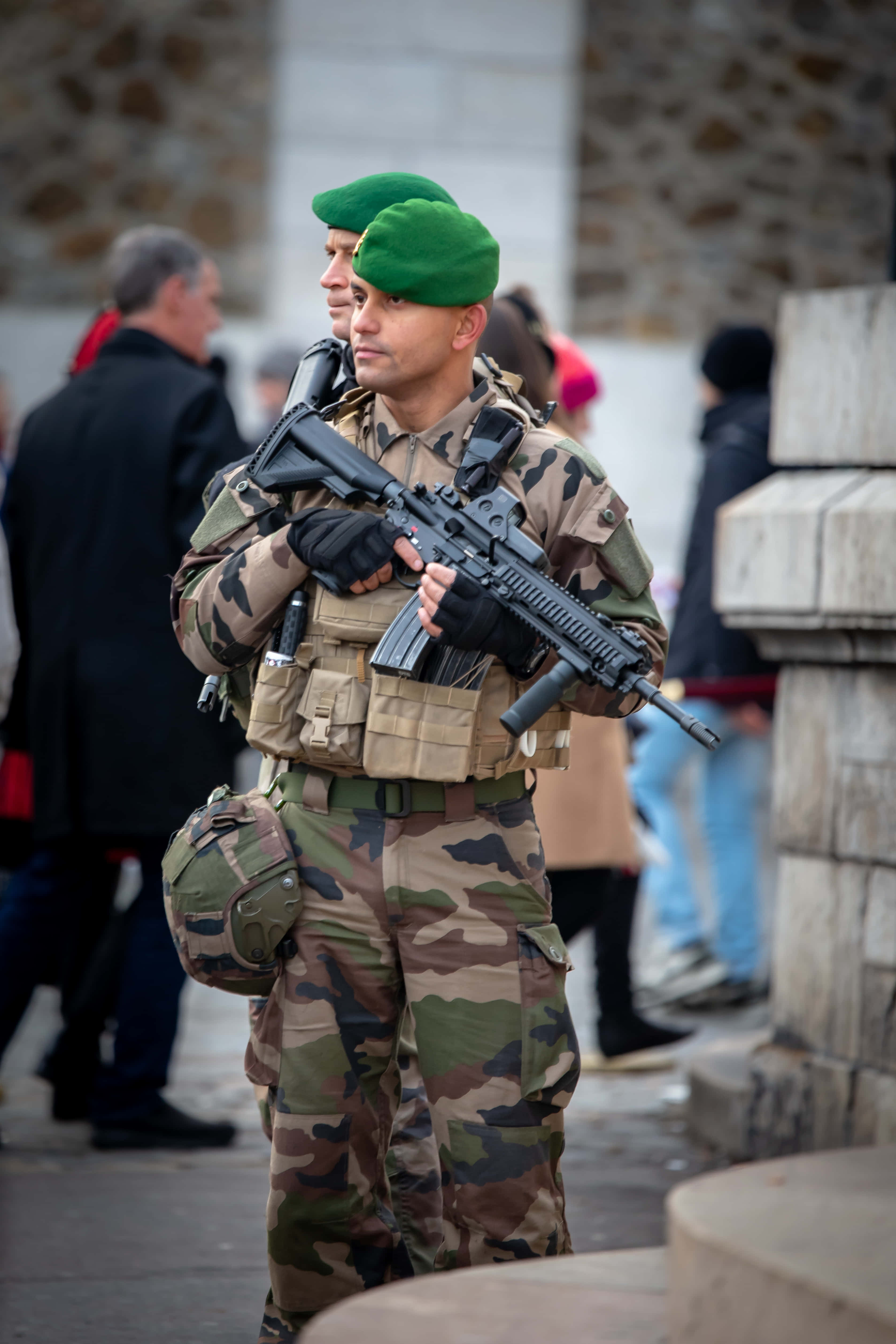 軍事動圖 桌布 壁紙 — 一名身穿迷彩服和綠色貝雷帽的士兵在石砌的城市街道上警覺地握著突擊步槍。