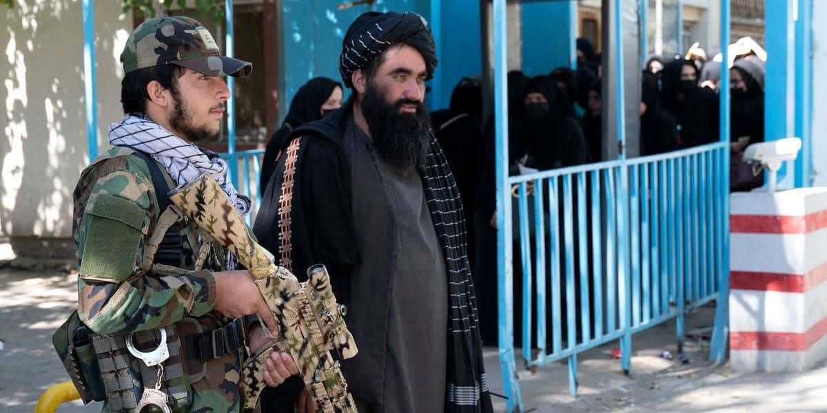 Taliban 桌布 壁紙 — 一名身穿迷彩服的士兵和一名身穿黑衣的鬍鬚男子站在藍色門外，身後有戴黑色面紗的女子在等候。