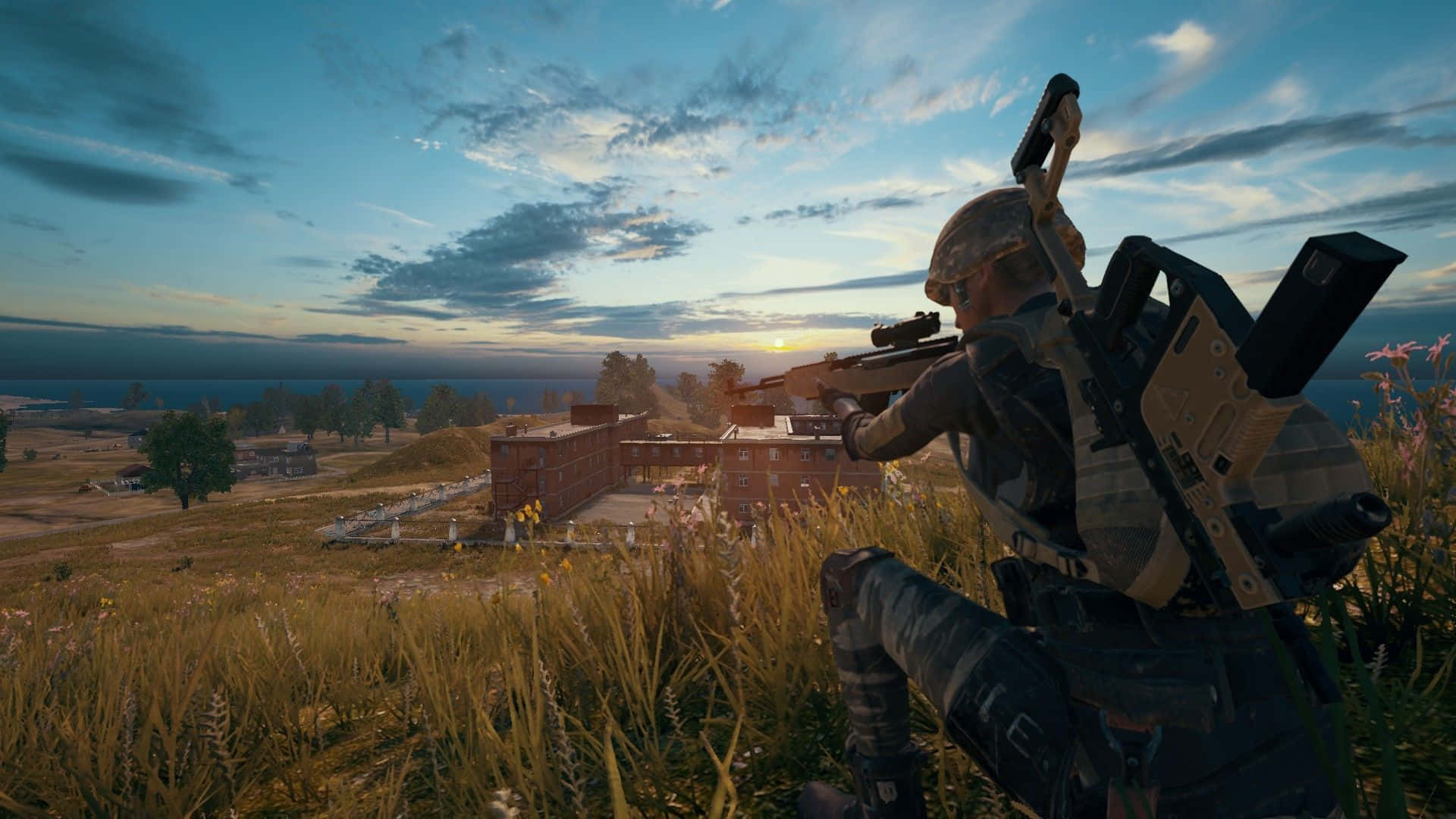 video games 桌布 壁紙 — 一名身穿迷彩服的士兵蹲在高高的草叢中，在金色夕陽下用步槍瞄準遠處的建築物。