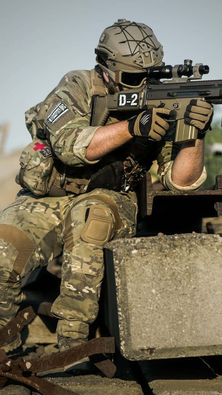 印度軍隊 桌布 壁紙 — 一名身穿迷彩裝備的士兵在陽光明媚的沙漠環境中，從混凝土屏障後方瞄準步槍。