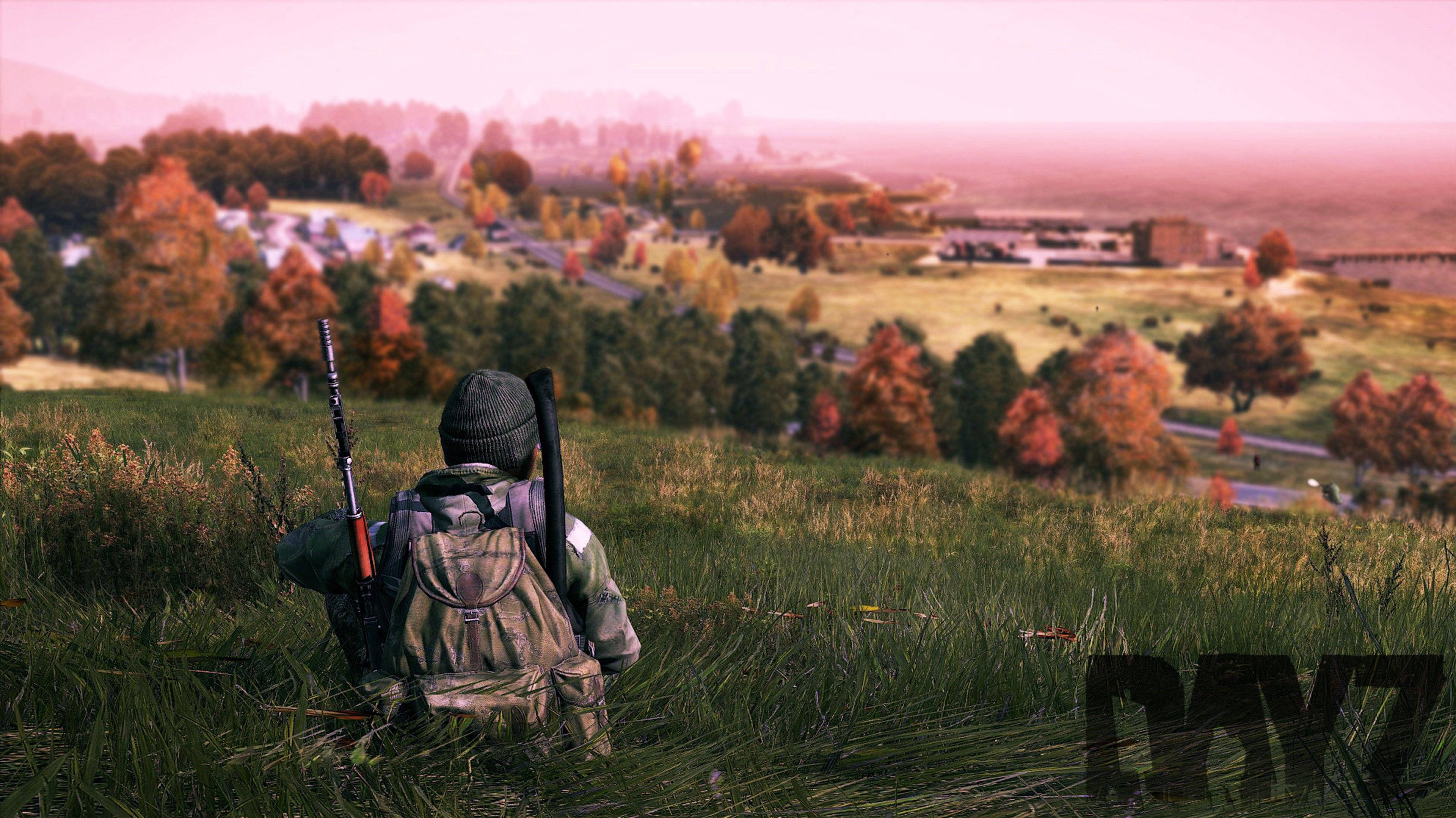 Dayz Desktop 桌布 壁紙 — 一名身穿迷彩裝備的士兵跪在草坡上，俯瞰著一個霧氣瀰漫的秋日村莊，村莊裡有色彩繽紛的樹木，天空呈現粉紅色。
