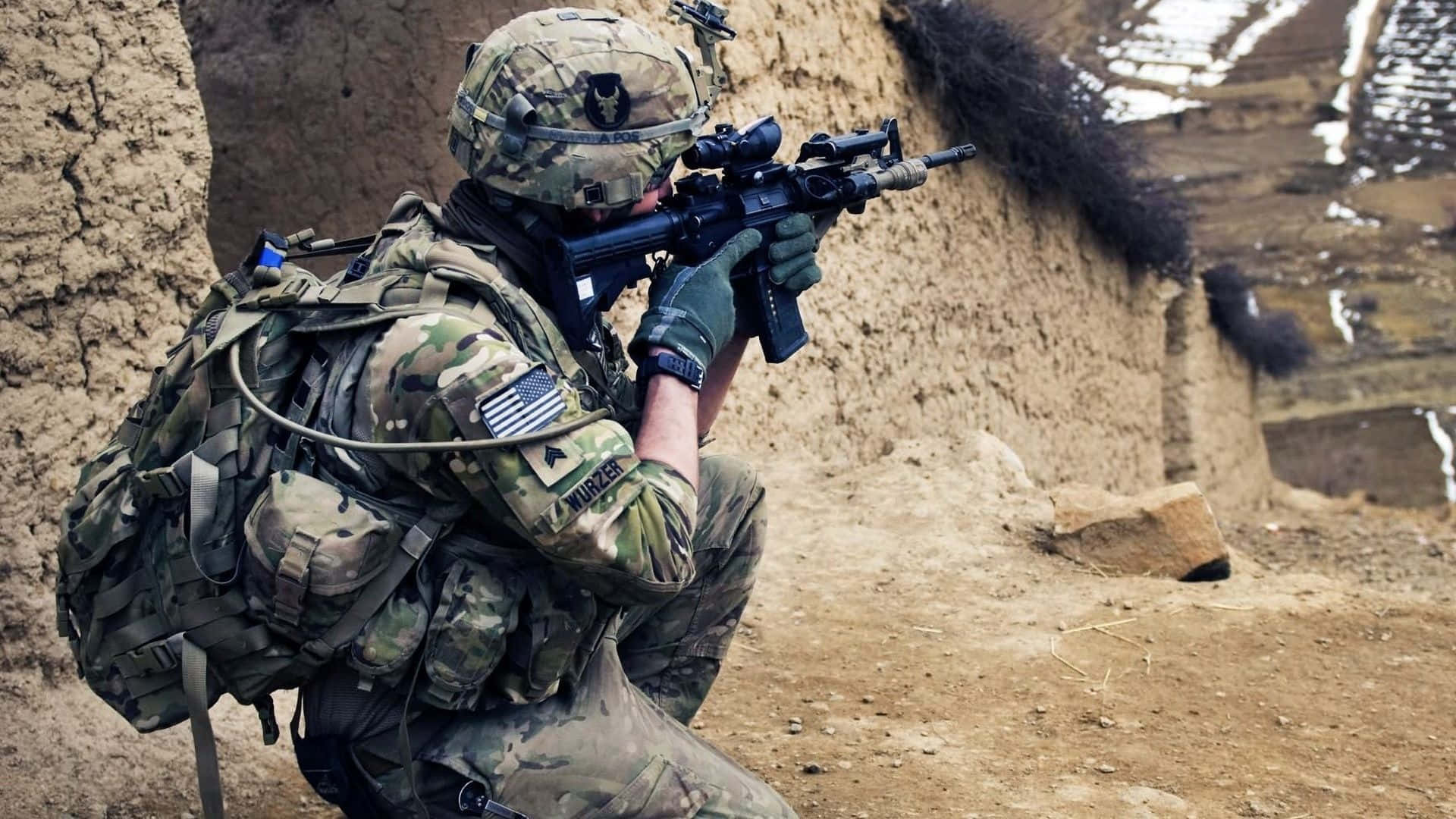 United States 桌布 壁紙 — 一名身穿迷彩裝備的士兵蹲在土堤後面，在崎嶇的戶外環境中瞄準步槍。