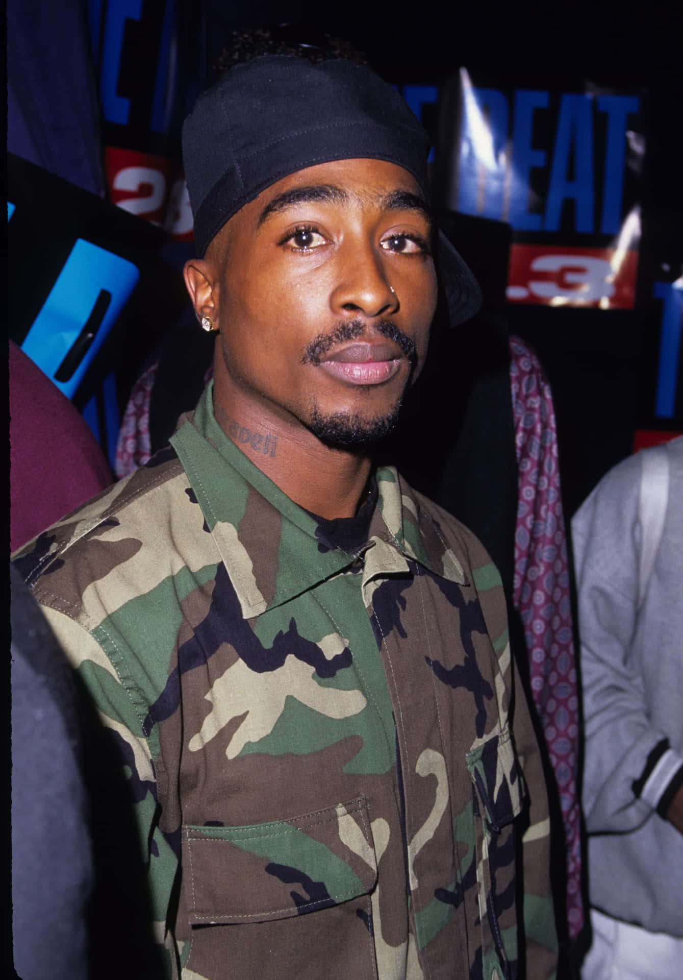 男子在音樂活動中穿著迷彩襯衫和黑色鴨舌帽。 — Tupac GIF 壁紙
