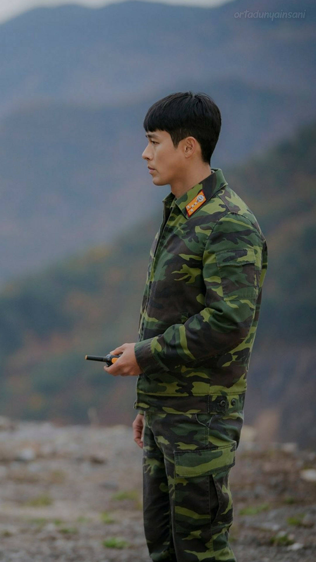 演員 桌布 壁紙 — 一名身穿迷彩軍服的士兵獨自站在岩石山坡上，俯瞰霧氣繚繞的山巒，手持無線電。