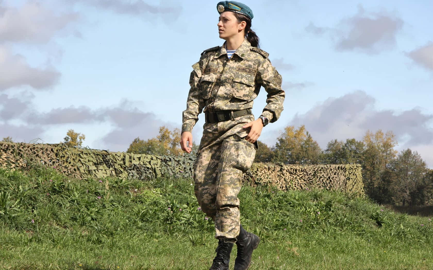Marines 桌布 壁紙 — 一名身穿迷彩軍服的女兵在部分多雲的天空下自信地走過草地。