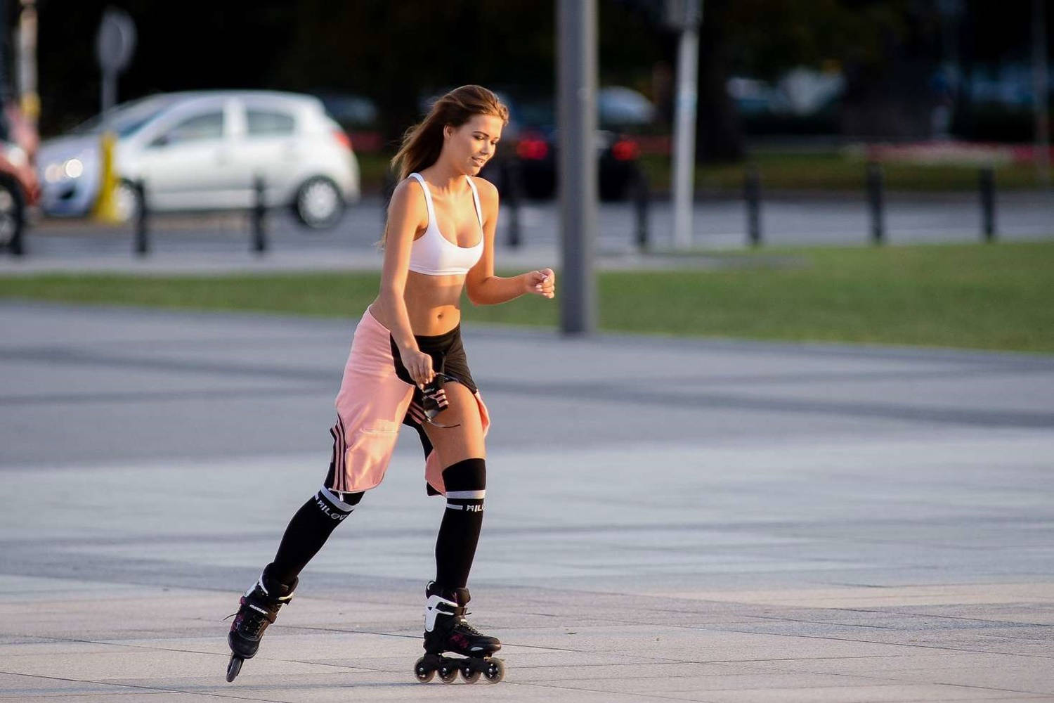 skating 桌布 壁紙 — 一名身穿運動裝備的女性在黃金時段於鋪砌的城市廣場上滑直排輪，背景中汽車模糊不清。