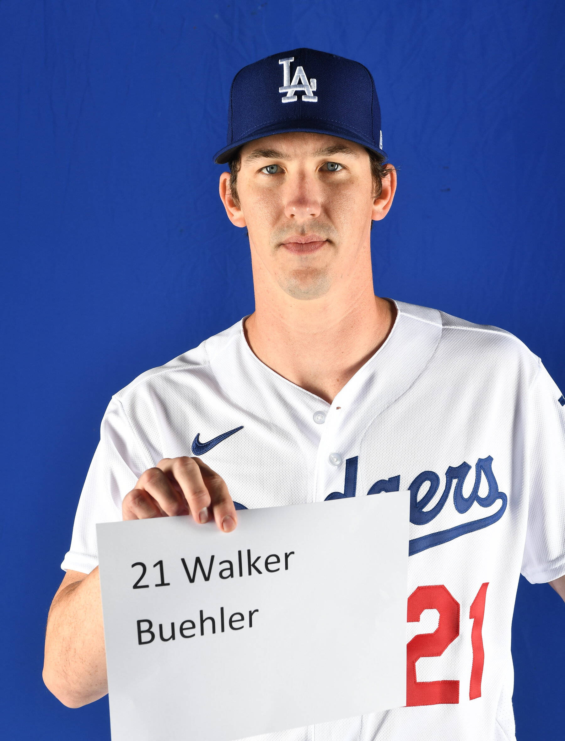 walker buehler 桌布 壁紙 — 一名身穿道奇隊球衣的棒球運動員在純藍色攝影棚背景前舉著寫有自己名字和號碼的牌子。