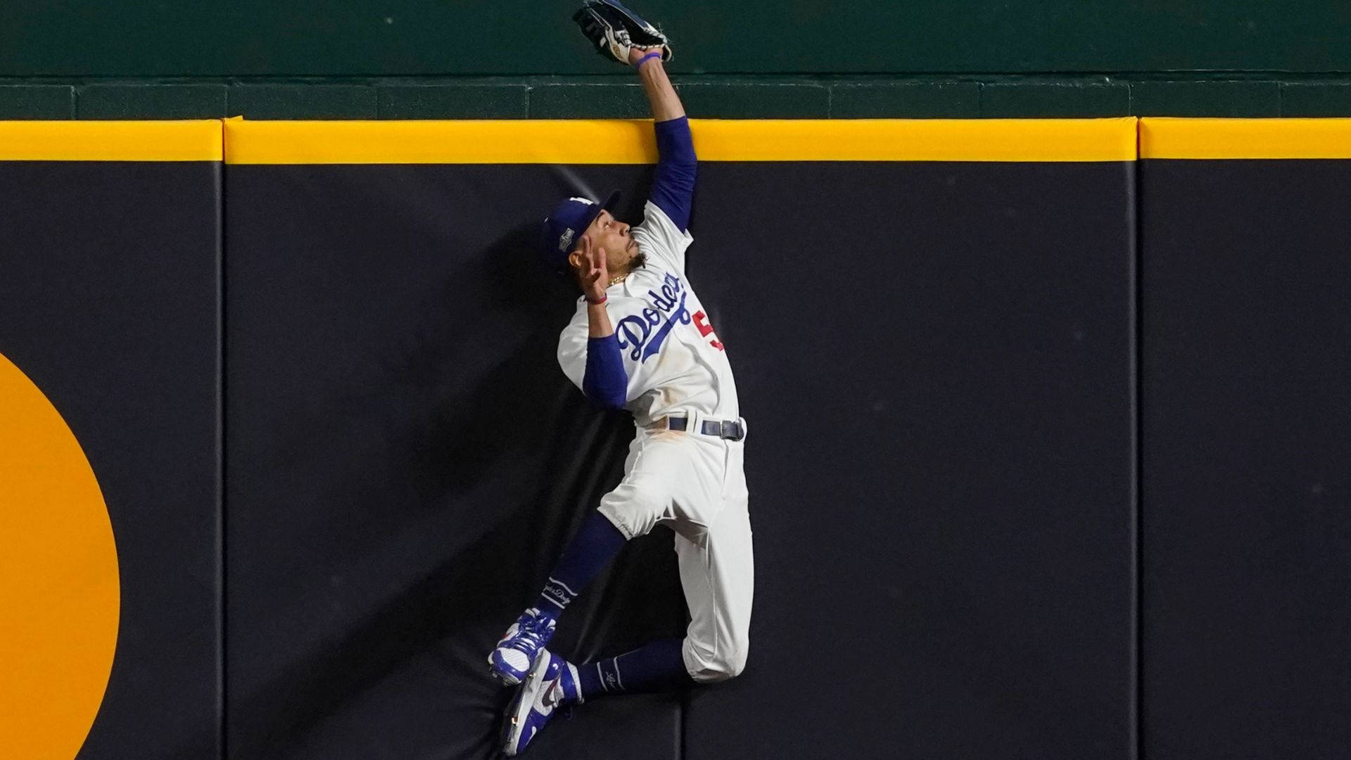 Mookie Betts 桌布 壁紙 — 一名身穿道奇隊球衣的棒球選手，跳向帶有黃色飾邊的深色牆壁接球。