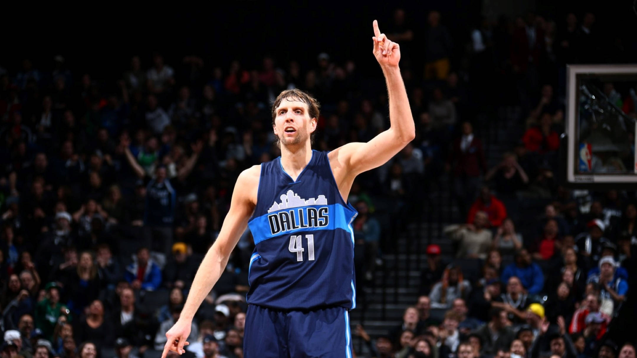 Dirk Nowitzki 桌布 壁紙 — 一名身穿達拉斯41號球衣的籃球運動員在明亮的場館燈光下比賽時，充滿強度地向上指。
