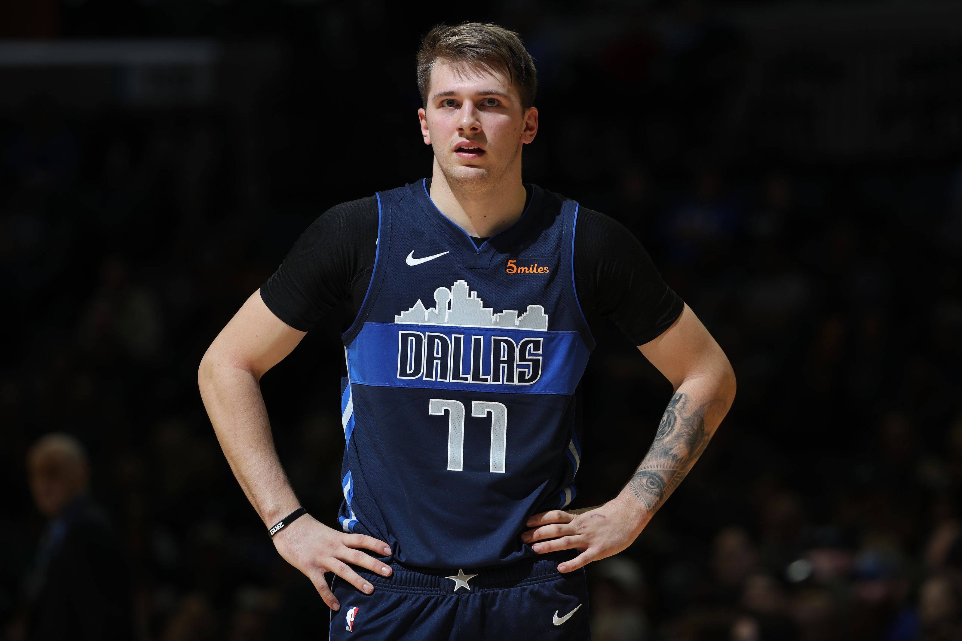 Luka 桌布 壁紙 — 一名身穿達拉斯獨行俠球衣的籃球運動員在明亮的場館燈光下，雙手叉腰站在比賽中。